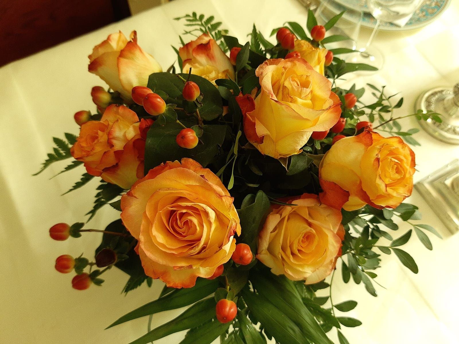 Bó hoa hồng vàng điểm quả hypericum đỏ đặt trên bàn tiệc